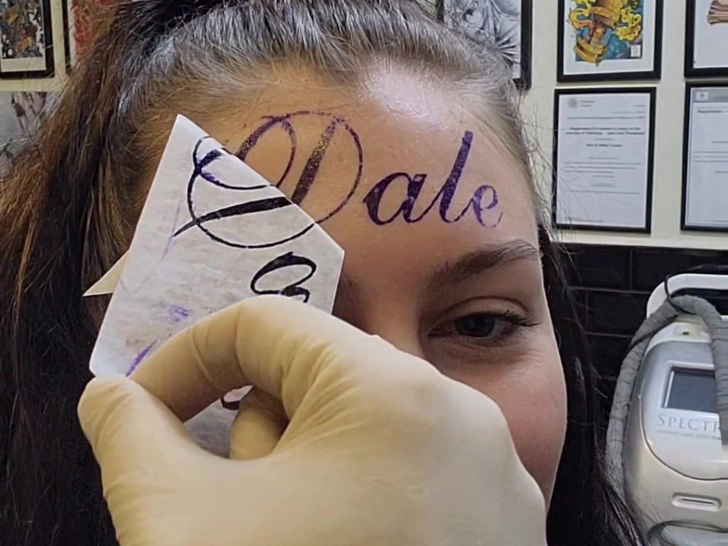 Mädchen lässt sich den Namen ihres Freundes auf die Stirn tätowieren (zeigt aber tatsächlich das Make-up)